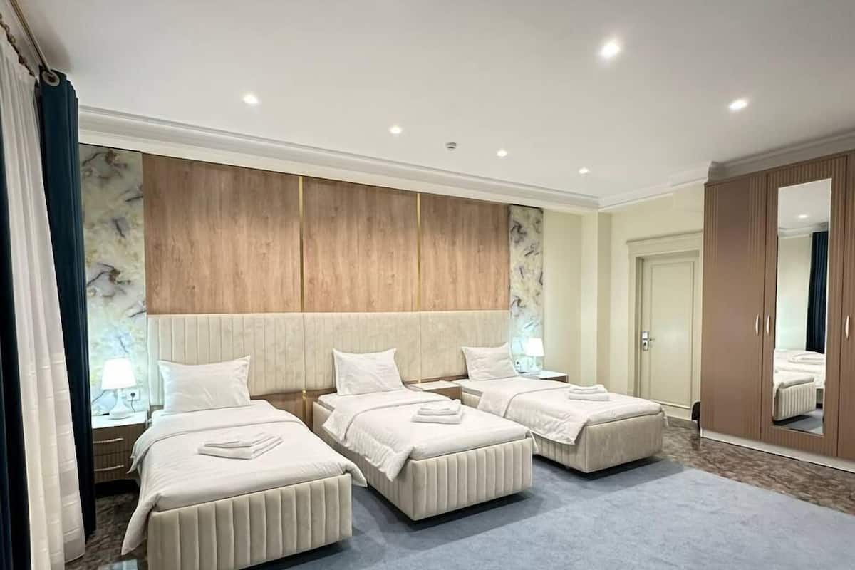 Una habitación de hotel con tres camas, un espejo grande y un armario.