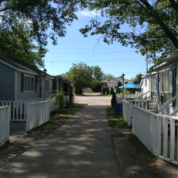 Une rue étroite bordée de maisons mobiles aux balustrades blanches, un ciel dégagé et, au loin, un parasol bleu.