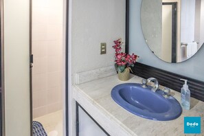 A bathroom with a blue sink, a mirror, and a vase with pink flowers. - Las Palmas (Mazatlán)