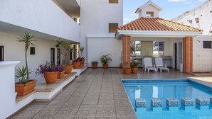 Une piscine avec un revêtement de sol en carrelage, des plantes en pot et des espaces de détente en plein air.