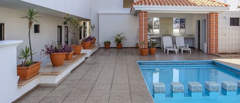A swimming pool with tiled flooring, potted plants, and outdoor seating.