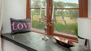 Ein Fenster mit Blick auf eine grüne Landschaft, ein Kandelaber, ein dekoratives Kissen mit dem Wort "LOVE" und eine kleine Pflanze.