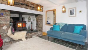 Ein gemütliches Wohnzimmer mit Kamin aus Stein, einem blauen Sofa und einem flauschigen weißen Hund.