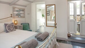 Ein Schlafzimmer mit einem Bett, einem Nachttisch, einer Lampe, einem Spiegel und Blick ins Badezimmer durch eine offene Tür.