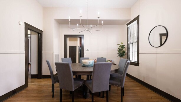 Un coin repas comprenant une table ronde, six chaises, un lustre et une plante en pot.