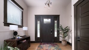 Un couloir avec une porte en bois sombre, un tapis coloré, un bureau avec une lampe et une plante en pot.