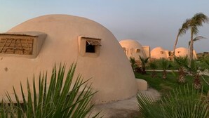 A series of dome-shaped buildings with small windows and a grassy area with palm trees.
