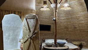 A rustic interior with a round table, wicker chairs, a woven ceiling, and a wooden door.