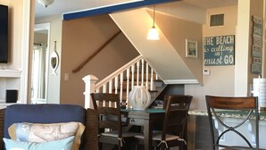 A dining area with a wooden table and chairs, a hanging light fixture, and a staircase leading to an upper level. - Oceanview, Updated, Wi-Fi , Pool.  Family Unit for 6 -  Must be 25+ to rent. (Matagorda)
