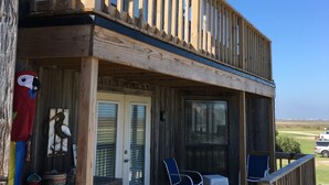 A wooden deck with a covered porch, a small table, two chairs, and a birdhouse. - Oceanview, Updated, Wi-Fi , Pool.  Family Unit for 6 -  Must be 25+ to rent. (Matagorda)