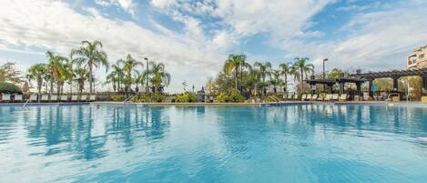 Una piscina con sillones de descanso y palmeras.