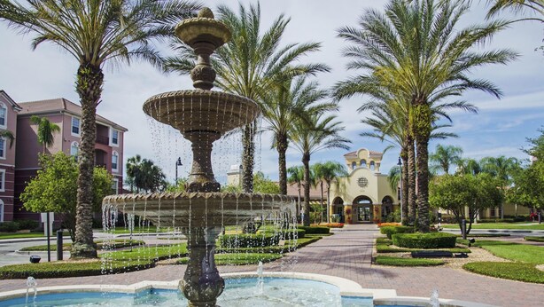 A fountain with multiple tiers and water jets, surrounded by palm trees and a well-maintained garden.