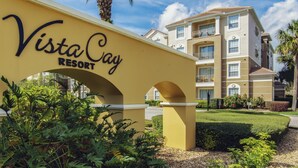 A yellow archway with the text "Vista Cay Resort" indicating the entrance to a multi-story building with balconies and a well-maintained lawn.