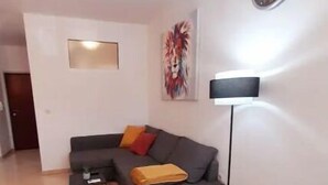 Una sala de estar con un sofá gris, una mesita de centro pequeña, una lámpara de pie y un tapete de colores con forma de cubo.