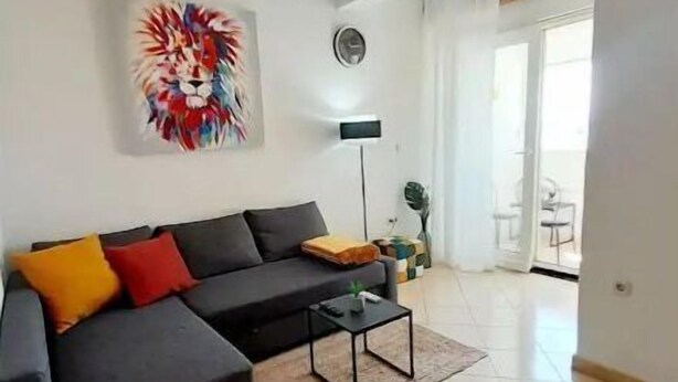 Una sala de estar moderna con un sofá seccional, una mesa de centro y una lámpara de pie. Hay un ventanal y una puerta que da a un balcón.