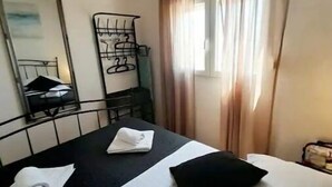Habitación de hotel con cama, escritorio y silla. Se observa una ventana con cortinas, un espejo y un estante en la pared.