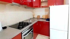 Una cocina con armarios rojos, un refrigerador blanco, una estufa y un lavamanos.