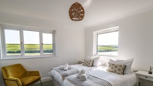 Un dormitorio con dos camas, una silla amarilla y vistas a campos verdes por las ventanas.