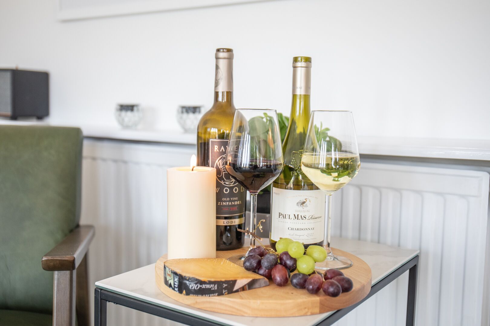 Une table avec deux bouteilles de vin, une bougie et une planche à fromage garnie de raisins.