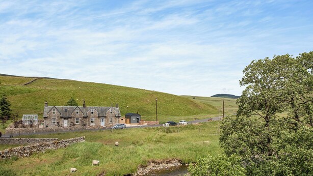 A rural landscape with a stone house, a stream, and a grassy hill. - The Liddel Dutch Barn - UK44465 (Saughtree, near Kielder)