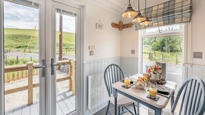 A dining area with a table set for two, a window with a plaid blind, and a view of a green landscape. - The Liddel Dutch Barn - UK44465 (Saughtree, near Kielder)