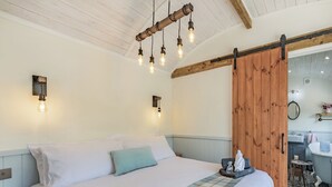 A bedroom with a large bed, a wooden door, a bathroom with a sink and mirror, and a ceiling with exposed beams. - The Liddel Dutch Barn - UK44465 (Saughtree, near Kielder)