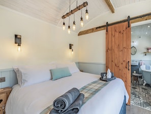 A bedroom with a large bed, a wooden door, a bathroom with a sink and mirror, and a ceiling with exposed beams. - The Liddel Dutch Barn - UK44465 (Saughtree, near Kielder)