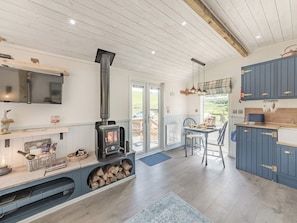 A modern kitchen with a wood-burning stove, a dining area, and a TV mounted on the wall. - The Liddel Dutch Barn - UK44465 (Saughtree, near Kielder)