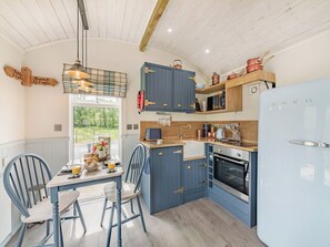 A kitchen with blue cabinets, a white refrigerator, and a dining area with two chairs and a table. - The Liddel Dutch Barn - UK44465 (Saughtree, near Kielder)