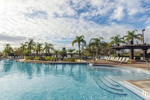 Una piscina con agua azul cristalina, rodeada de palmeras y sillas de descanso.