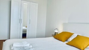 A neatly made bed with white and yellow pillows, a stack of folded towels, and a white wardrobe with a mirror. - 2 bedrooms with Terrace and Parking (Luxembourg City)