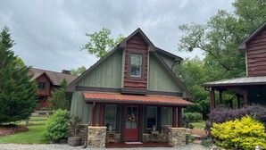Une maison à deux étages avec une porte d’entrée rouge, des fondations en pierre et un porche couvert.