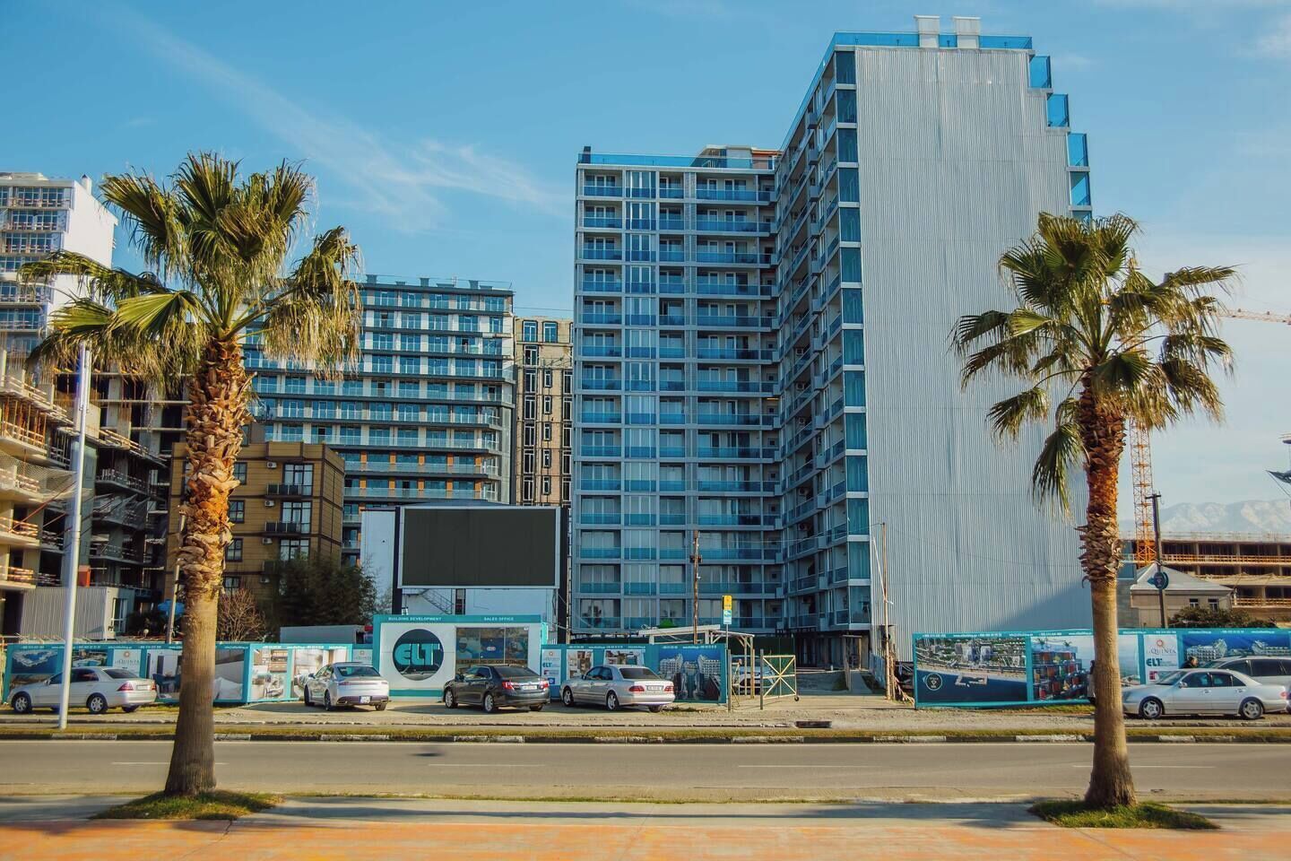 Un moderno edificio de gran altura con varios pisos, rodeado de palmeras y otros edificios.