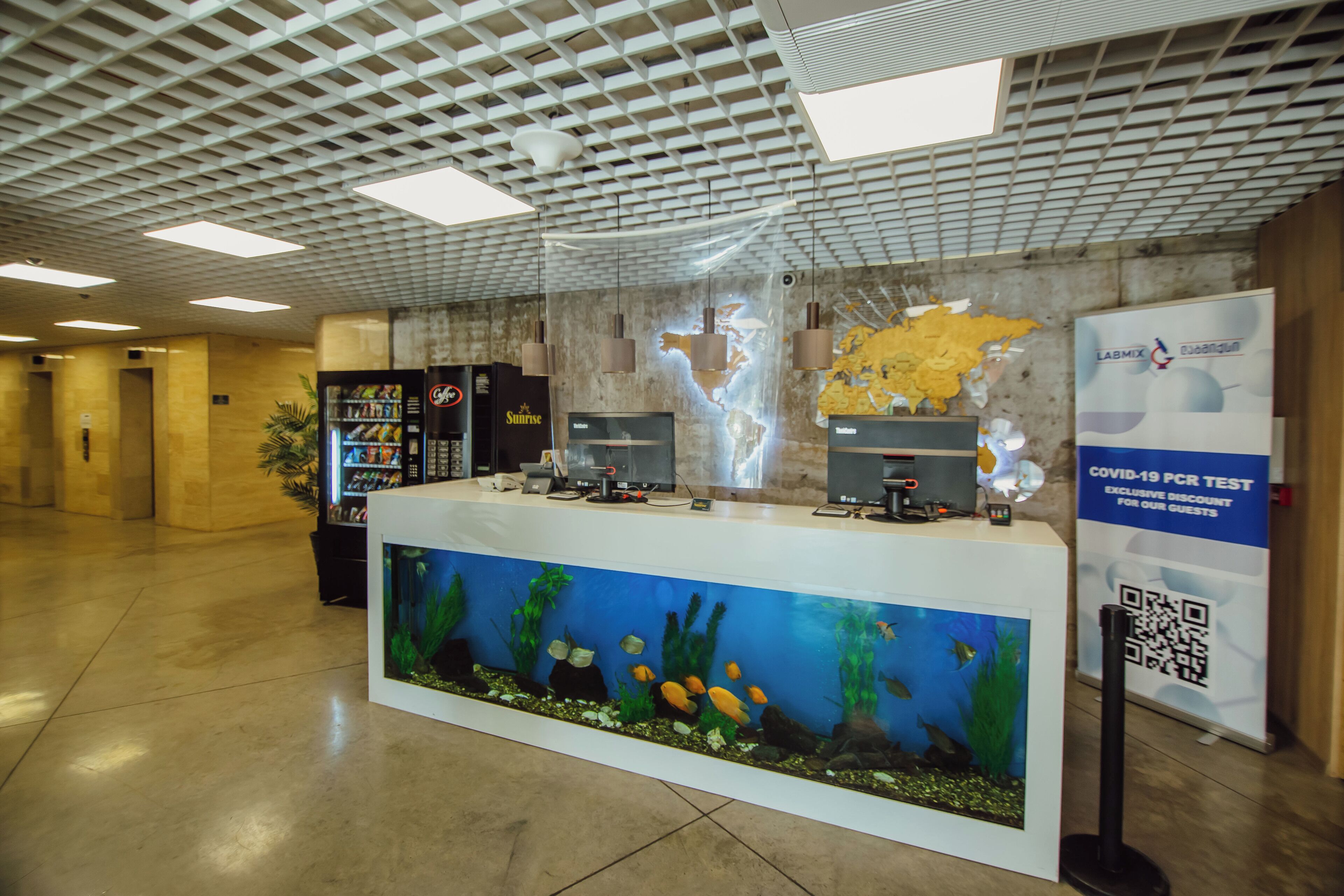 A reception area with a large aquarium display, a map on the wall, and a COVID-19 PCR test sign.