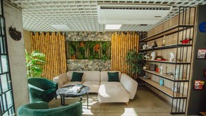 A modern living room with a sectional sofa, a round coffee table, and a green armchair. There is a bamboo wall divider and a bookshelf with various items. - Lovely Studio in Batumi With Rooftop in Building (Batumi)