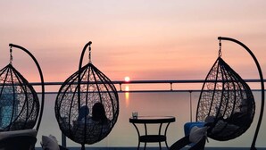 A sunset view from a balcony with hanging chairs and a table. - Lovely Studio in Batumi With Rooftop in Building (Batumi)