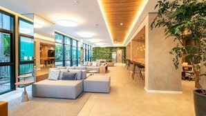 A spacious, modern lounge area with a long bench seating arrangement, a small round table, and a large potted plant. - Is Moema (São Paulo)