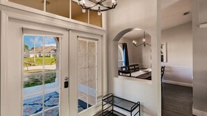 Uma entrada espaçosa com uma grande porta de vidro, um banco e um lustre.