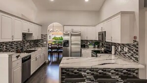 Cozinha moderna com armários brancos, uma ilha de mármore e painel de fundo padronizado.