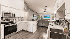 Uma cozinha moderna com armários brancos, uma ilha grande, eletrodomésticos de aço inoxidável e vista para a sala de estar.