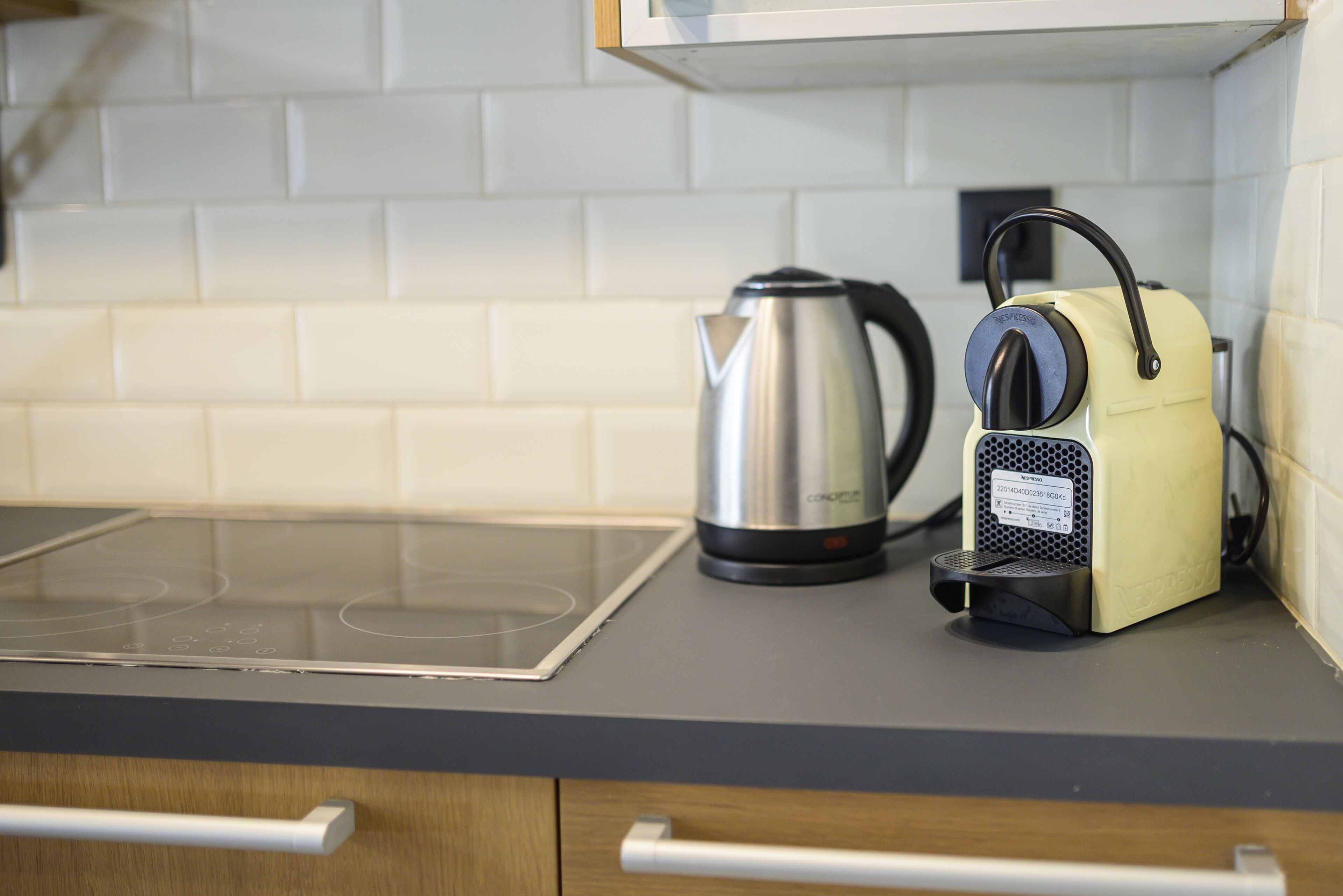 A kitchen with a modern induction cooktop, a stainless steel kettle, and a yellow electric kettle on the counter.
