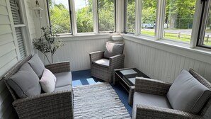 Aurinkoinen huone, jossa on rottinkihuonekaluja, sininen matto ja suuret ikkunat, joista avautuu näkymä ulkona olevaan vehreään maisemaan.