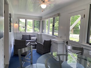 Relax in a sunroom with a sofa, two chairs, and a glass table, surrounded by lush views.