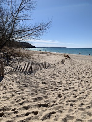A sandy beach with footprints, a wooden fence, and a clear blue sky. - Classic Cottage in the Heart of Leland (Leland)