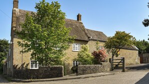 A stone house with a thatched roof, a wooden gate, and a paved driveway.