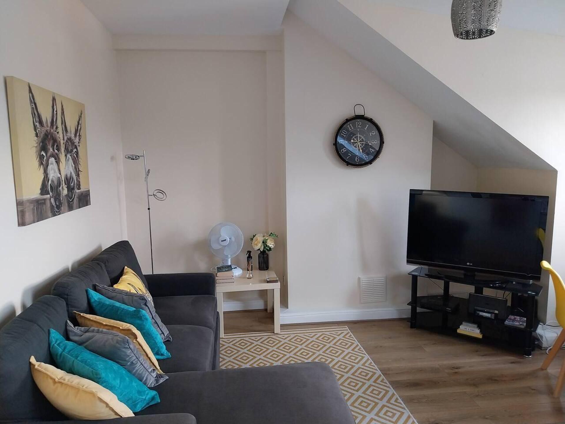 Ein modernes Wohnzimmer mit grauem Sofa, einem Flachbildfernseher, einem Deckenventilator und einem Gemälde an der Wand.