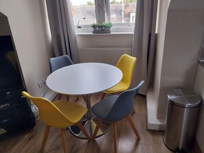 A small dining area with a round table and four chairs, a radiator, a window with plants, and a trash bin. - Leeds Cute 1 bed Apt, Garden, Free Wifi & Parking (Leeds)