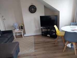 A modern living room with a flat-screen TV, a dining table with chairs, a patterned rug, and a clock on the wall. - Leeds Cute 1 bed Apt, Garden, Free Wifi & Parking (Leeds)