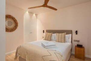 A neatly made bed with a folded towel, a wooden nightstand, a wall-mounted mirror, and a ceiling fan.