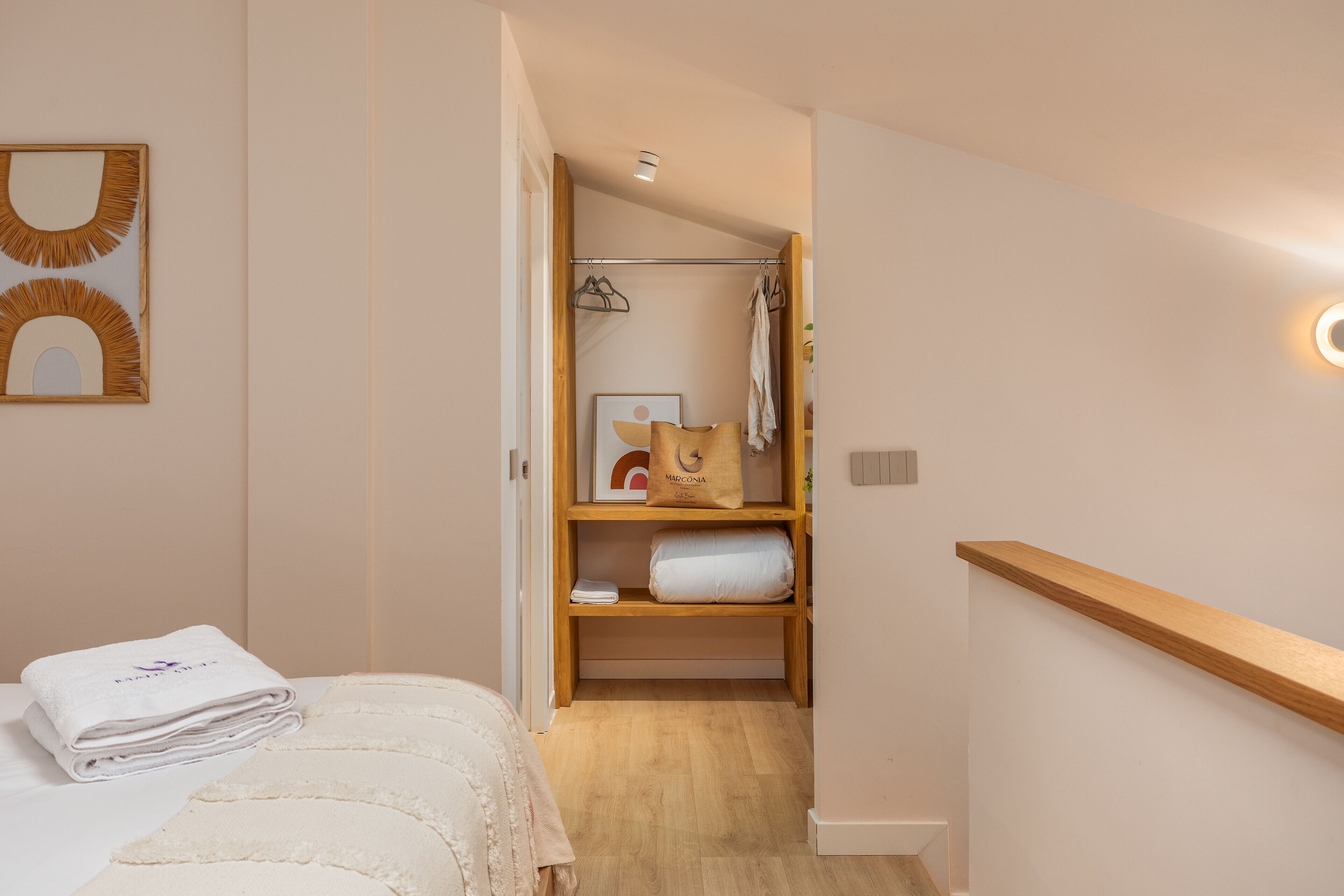 Une chambre à coucher comprenant un lit, une table de chevet, une étagère en bois avec des serviettes et une armoire avec des vêtements suspendus.